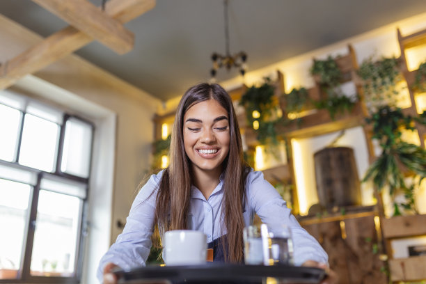 快乐的女服务员端着咖啡托盘，在自助餐厅工作，为桌子服务图片下载