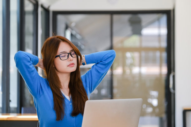 年轻的亚洲女子坐在椅子上扭动身体放松。图片下载