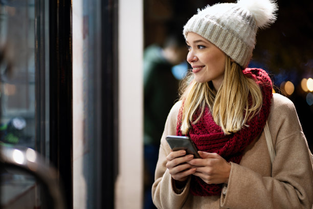 年轻美丽的女子使用她的手机上网与智能手机在一个冬天的一天在城市图片下载