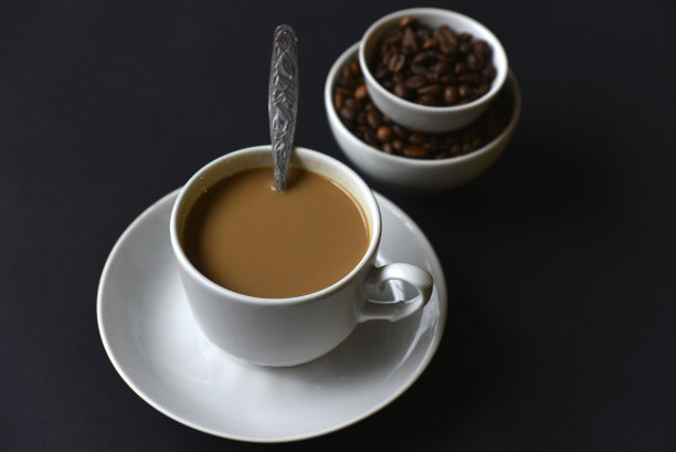 美味的咖啡盛在瓷杯里，配上茶托和咖啡豆。咖啡在杯子里，豆子在黑色的背景上。图片下载