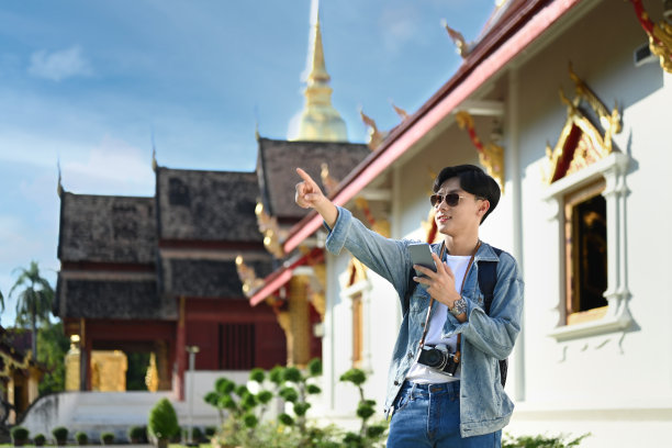 年轻的亚洲游客站在美丽的佛寺宝塔上用智能手机寻找方向。图片下载
