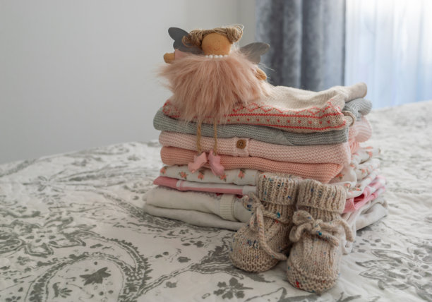 一堆粉色和灰色调的儿童服装，一个天使玩具和灰色和白色背景的手工针织童鞋。新生儿用天然材料制作的衣服。图片下载