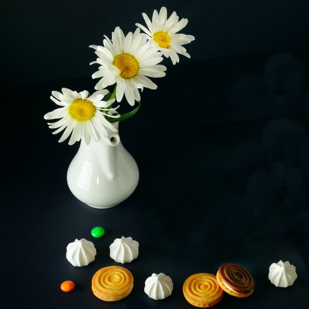 饼干、蛋白霜和一束洋甘菊插在黑色背景的白色花瓶里。文本的空闲空间。图片下载