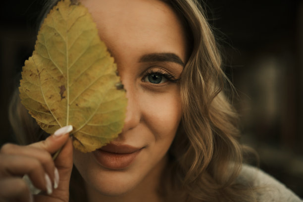 女孩看着镜头，用一片树叶合上一只眼睛图片下载