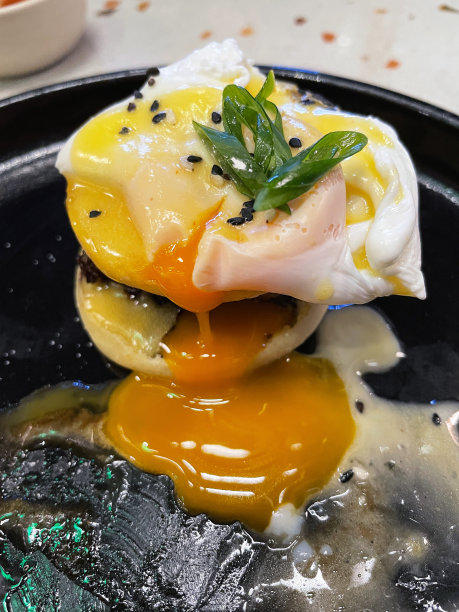 黑色盘子的特写图片与鸡蛋本尼迪克食谱堆叠分裂的英国松饼填充猪肉香肠，顶部与荷兰酱和荷包蛋渗出蛋黄，抬高视图图片下载