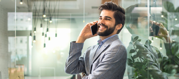 英俊的微笑商人在办公室打电话。图片下载