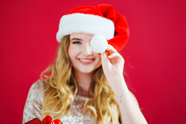 一个红色背景上戴着圣诞老人帽子的美丽女人。图片下载