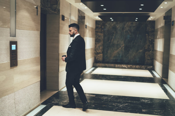 帅气的商人穿着正装，端着咖啡在办公室等电梯图片下载