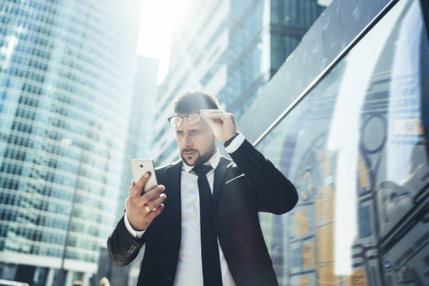 穿着正装的困惑商人在城市街道上用智能手机阅读新闻图片下载