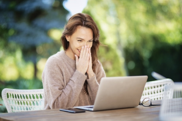 快乐的中年妇女使用笔记本电脑，而坐在家里的阳台上图片下载