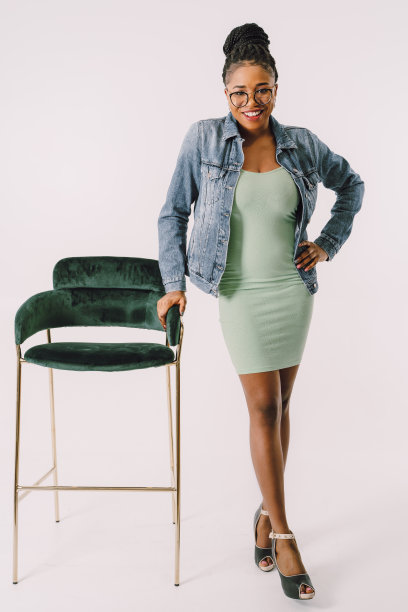 快乐的年轻女子在一件连衣裙牛仔夹克抱着椅子股票照片图片下载