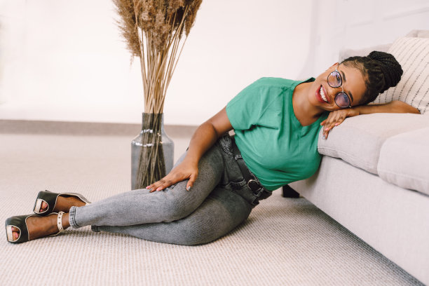 年轻的非裔美国妇女穿着t恤坐在客厅摆姿势，手和头在沙发上的股票照片图片下载