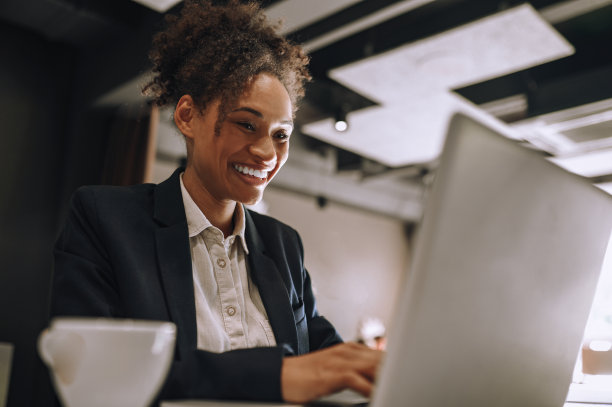 微笑的女人在办公室的笔记本电脑上打字图片下载