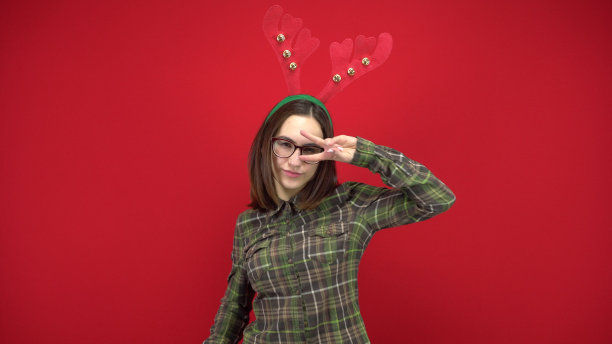 一名年轻女子正戴着圣诞鹿角形状的发带跳舞。工作室拍摄，红色背景。图片下载