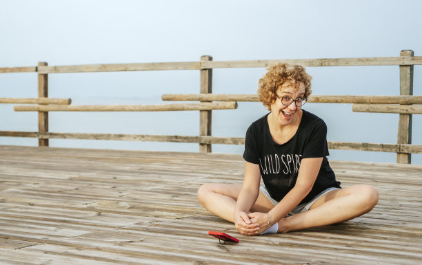 一名成年女子在海边的一个码头上用手机练习拉伸和瑜伽姿势。心理健康概念图片下载