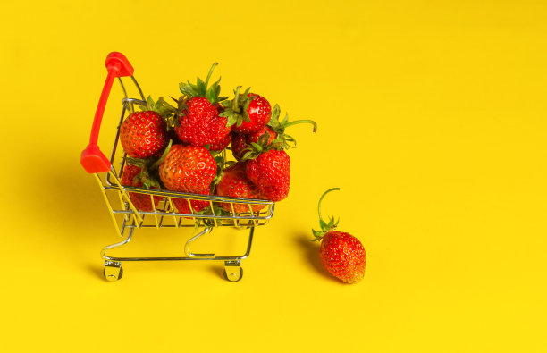 黄色背景的推车里的新鲜草莓。快乐购物理念。免费广告位图片下载