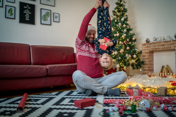 在黑暗的客厅里，父亲在圣诞树和舒适的壁炉的背景下和快乐的孩子儿子玩耍图片下载