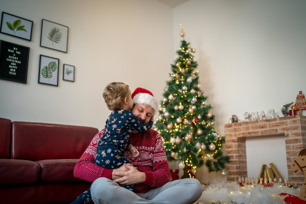在黑暗的客厅里，父亲在圣诞树和舒适的壁炉的背景下和快乐的孩子儿子玩耍图片下载