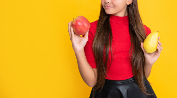 高兴的孩子拿着新鲜的苹果和梨在黄色的背景图片下载