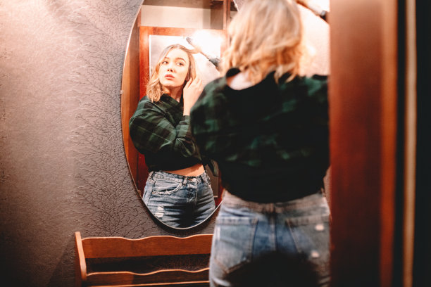 年轻女子在家里用卷发棒看着镜子里的自己，准备出门图片下载