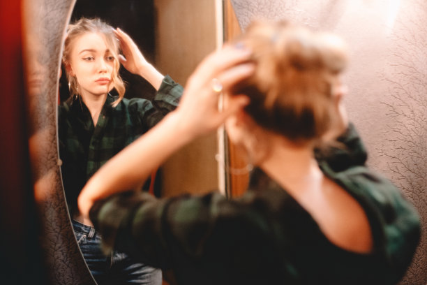年轻女子做头发，同时看着自己在镜子在家里准备出去图片下载