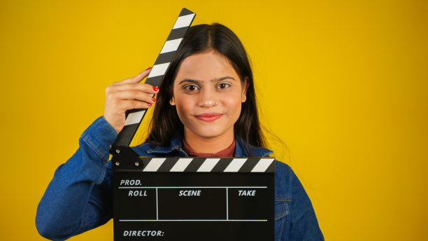 美丽的年轻亚裔印度女子站在手里拿着隔板，隔板用于电影制作，孤立在彩色背景的工作室肖像图片下载