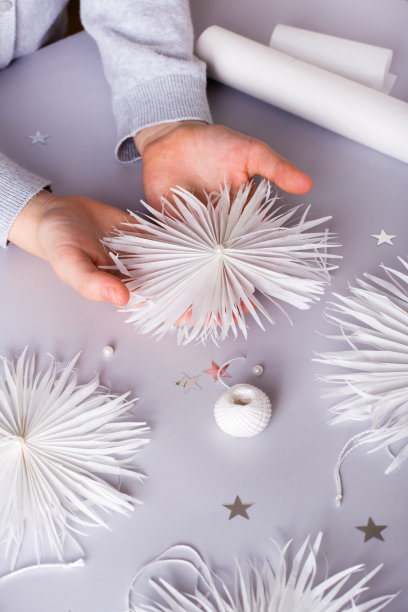 孩子们的手拿着一个纸雪花，上面有一根线和一颗珠子。手工制作的装饰。俯视图图片下载