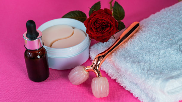 用眼罩包装。美容产品。粉色y型球滚轮供面部按摩和眼部绷带用毛巾放在桌上。自由空间。滚筒由玫瑰石英制成。图片下载