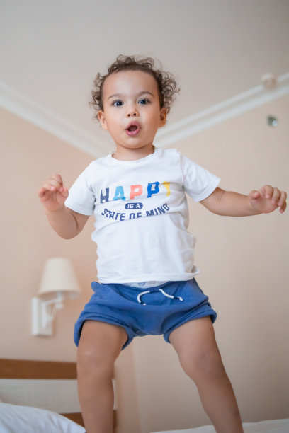 Curly蹒跚学步的男孩在床上蹦蹦跳跳，玩得很开心图片下载