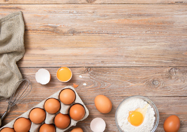 白色托盘，盛有生鸡蛋和蛋黄面粉，厨房毛巾放在木桌上。图片下载