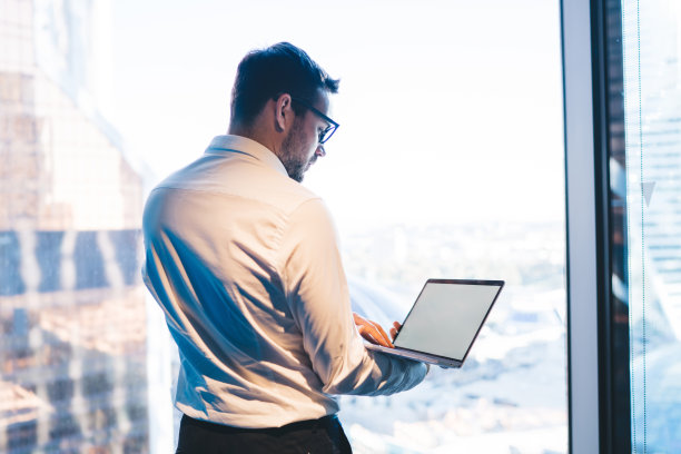 商人工作在笔记本电脑对窗户在办公室图片下载