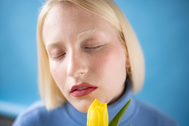 年轻的金发女子与黄色郁金香对蓝色背景。图片下载