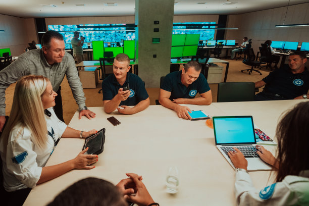 在系统控制室，一群保安坐在那里做简报，他们在安全数据中心工作，周围有多个屏幕图片下载