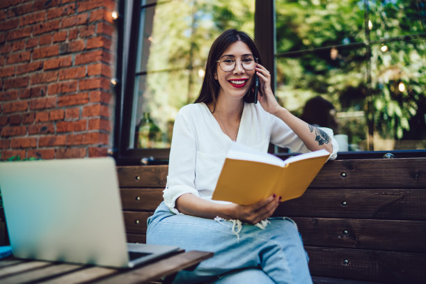 女性自由职业者坐在咖啡馆露台上，用现代上网本进行远程工作，通过手机应用程序打电话，快乐的女人拿着备忘录教科书，制定时间管理计划图片下载