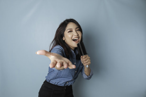 无忧无虑的亚洲女人的肖像，有乐趣卡拉ok，在麦克风唱歌，站在蓝色背景图片下载