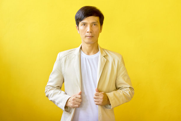 帅气的男人穿着时髦的夹克，手挽衬衫，自信地微笑，站在一个简单的背景前。图片下载