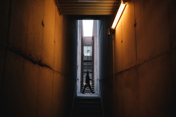 孤独的剪影走在现代混凝土建筑，橙色的灯光在前景。图片下载