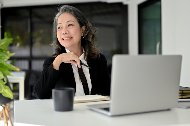 开朗的亚洲老年女商人做着白日梦，微笑着看着窗外。图片下载
