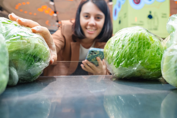 一名妇女正在寻找蔬菜，从货架上拿着产品，一对顾客拿着清单购物图片下载