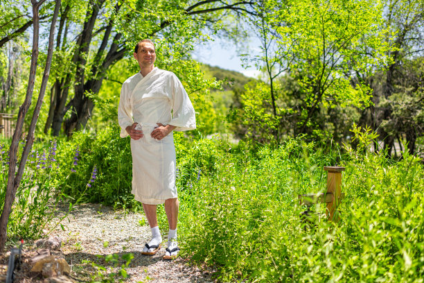 年轻快乐的男子穿着浴衣白袍温泉服装或长袍站在户外花园在日本与自然景观图片下载