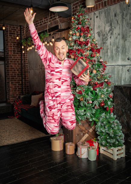 快乐有趣的快乐男子与圣诞礼物盒跳在装饰杉树附近图片下载