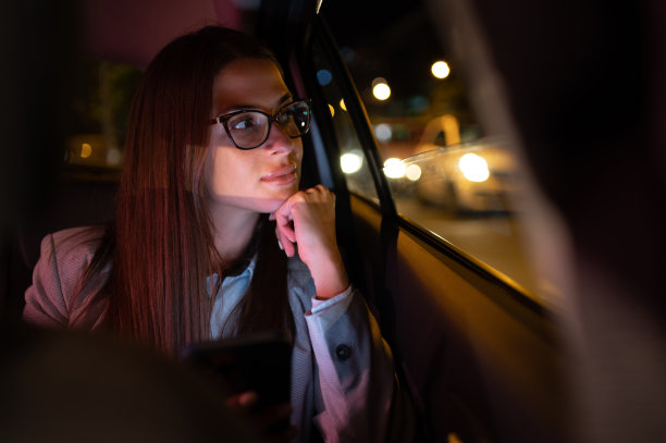 一位商务女性晚上坐在汽车后座上使用智能手机图片下载
