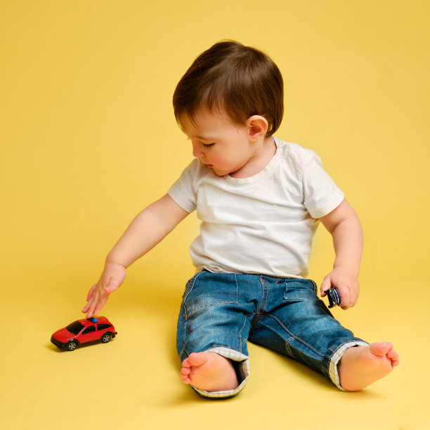 蹒跚学步的婴儿在工作室的黄色背景上玩玩具车。穿着白色t恤和蓝色牛仔裤的快乐孩子在玩玩具车。一岁四个月大的孩子图片下载