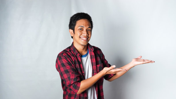 成年亚洲男子穿着红色法兰绒t恤指向右边区域，微笑的脸孤立的白色背景图片下载