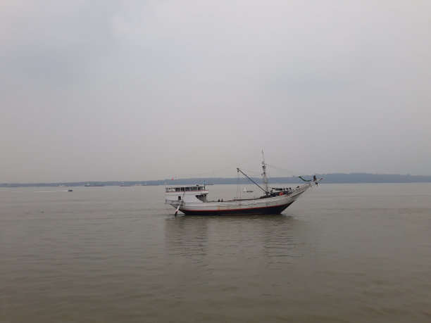 传统的木船在傍晚黑暗的天空下航行在棕色的海水中图片下载