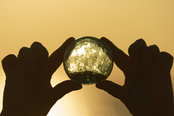 摄影的绿色与蓝色清晰水晶球在人类的手中在太阳面前。用玻璃浮子做网(咯咯叫)..金色的天空和波罗的海为背景。奇迹的观点。图片下载