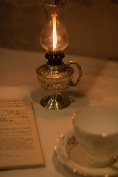 一盏煤油灯和一个空杯子和碟子的照片站在桌子上与一本打开的书图片下载