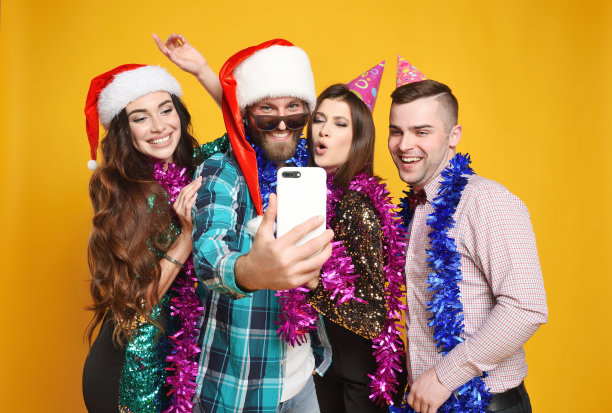 一群或一群朋友戴着圣诞帽，派对帽，博阿斯庆祝圣诞节，玩得开心，自拍，在黄色背景下直播。图片下载
