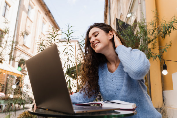 震惊的快乐女孩在赢了赌注，坐在户外咖啡馆的笔记本电脑。开朗惊讶的女人微笑，看着在网上赌场的收入收入数额和喜悦。图片下载