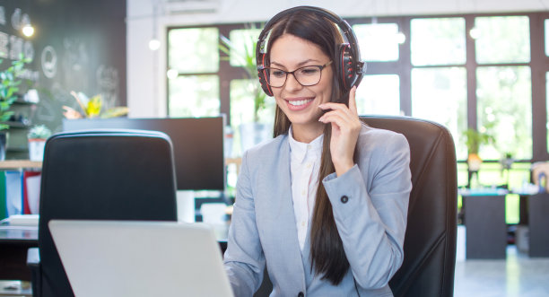 年轻的女商人戴着耳机在现代办公室的笔记本电脑上工作。图片下载